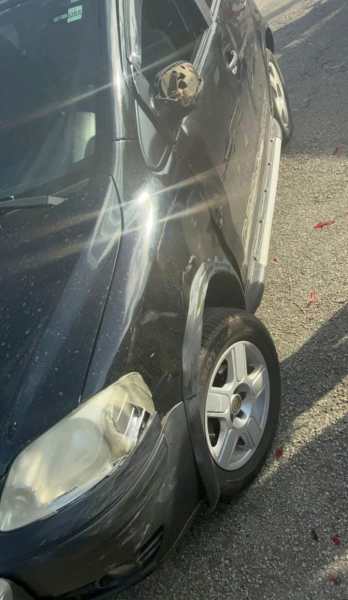 Carro preto estacionado com um dano visível na lateral e um pneu furado.