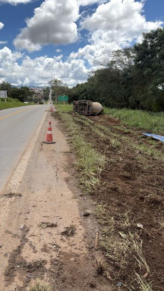 Caminho com um caminhão tombado ao lado da estrada, cercado por cones de sinalização e vegetação.