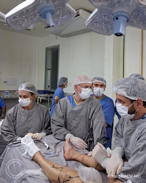Equipe médica em sala de cirurgia, com supervisores e assistentes em procedimentos médicos. O paciente está deitado na mesa de operação com o foco em um dos membros inferiores.
