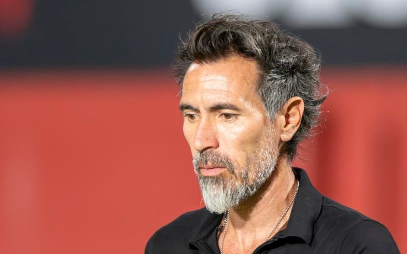 Close-up of a middle-aged man with a beard and short, wavy hair, wearing a black shirt and looking thoughtfully off-camera.