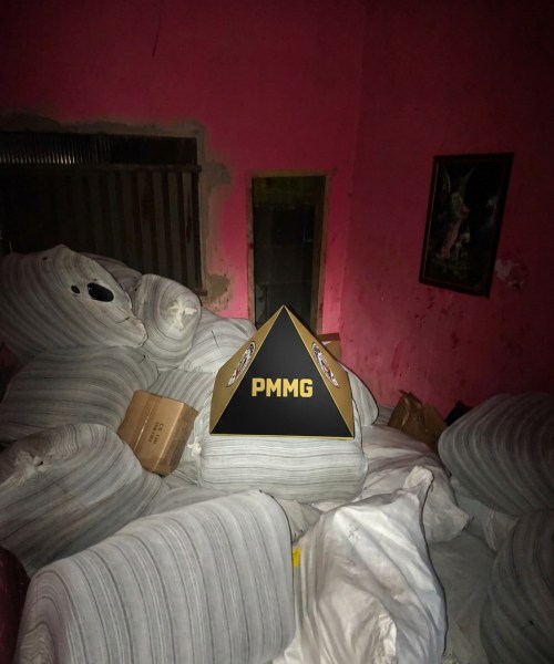 Um ambiente interno com paredes rosas, cheio de colchões e almofadas, onde se destaca um objeto piramidal com a sigla PMMG.