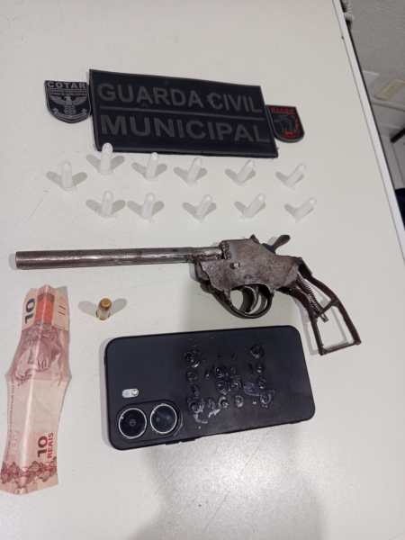 Imagem de objetos de apreensão, incluindo uma arma, um celular, uma nota de dez reais e distintivos da Guarda Civil Municipal.