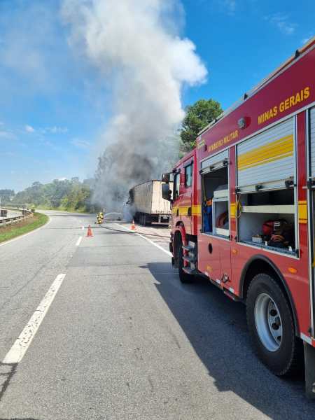 Caminhão pegando fogo na estrada, com fumaça saindo e um caminhão de bombeiros ao lado.