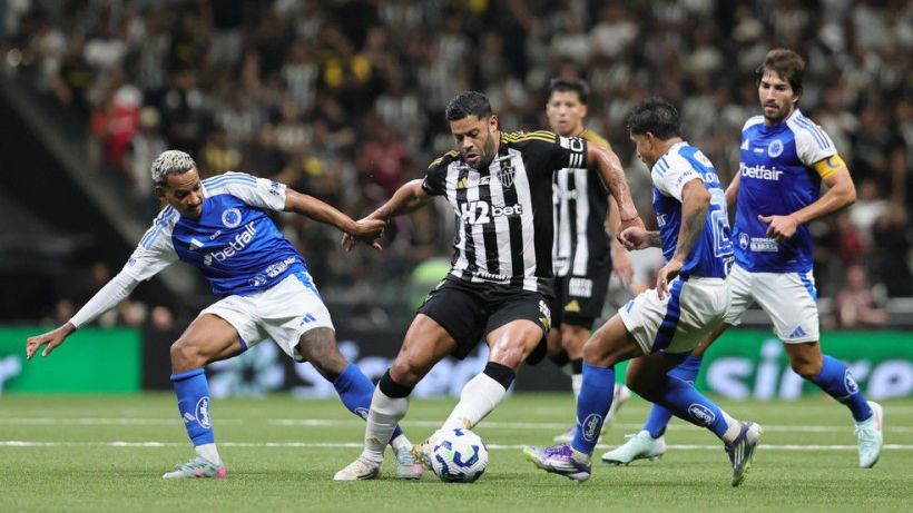 A soccer match scene featuring players in action, with a player in black and white stripes dribbling the ball surrounded by opponents in blue and white jerseys.