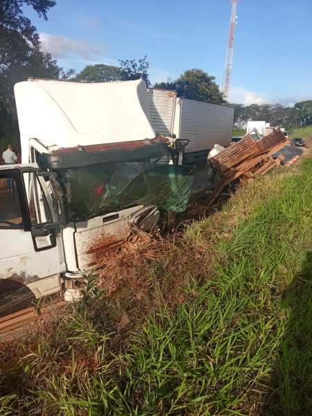 Caminhão acidentado na estrada, com a cabine danificada e carga de madeira espalhada ao lado