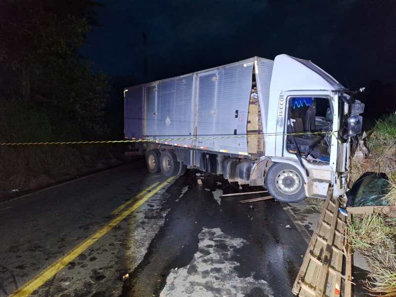 Caminhão tombado em estrada deserta à noite, sinalizando um acidente com danos visíveis e cercado por fita de segurança.
