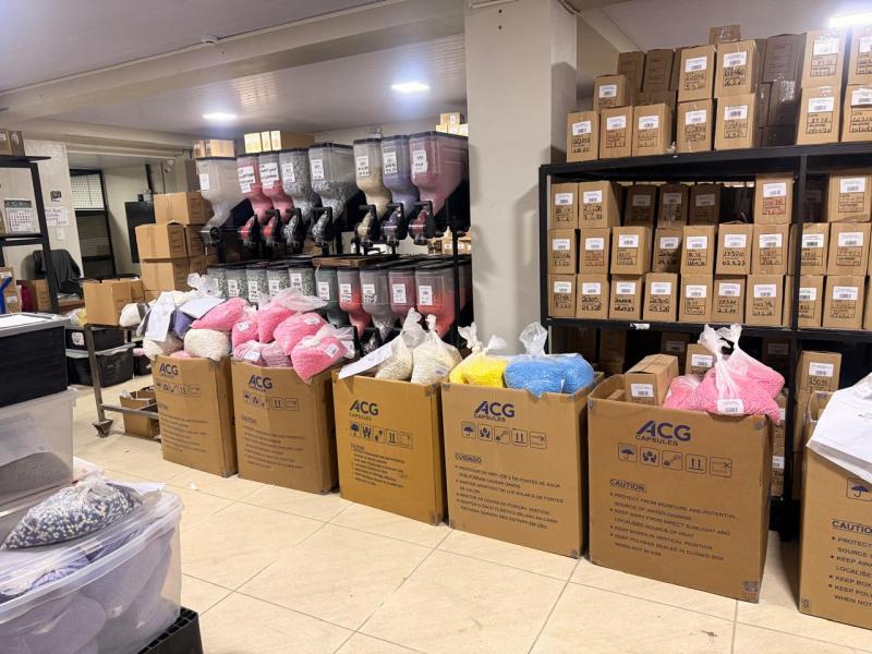 Armazém com caixas de papelão organizadas, contendo materiais coloridos em sacos plásticos, e prateleiras com silos em diferentes cores.