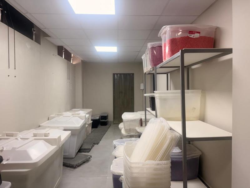 Interior de um depósito com prateleiras e recipientes plásticos organizados, incluindo diferentes tipos de caixas, alguns contendo produtos coloridos.