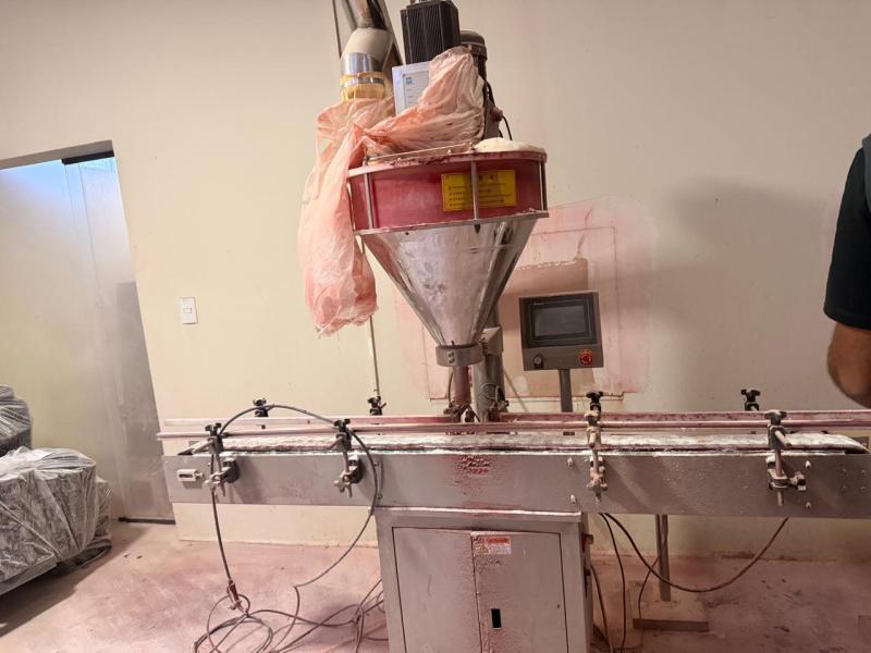 Máquina de envase com funil e display de controle em ambiente industrial.
