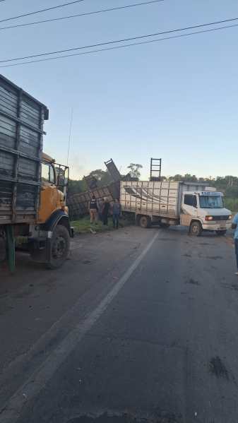 Caminhões parados na beira da estrada, com um deles tombado e pessoas trabalhando na remoção da carga.