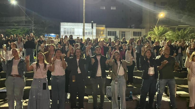 Público em um evento noturno, com pessoas em pé e braços levantados, mostrando envolvimento e celebração.