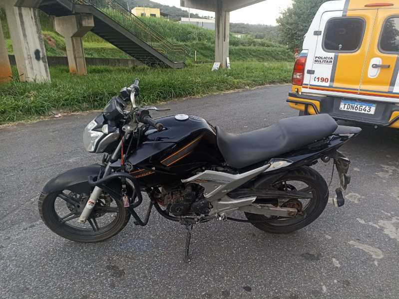 Motocicleta preta com detalhes em laranja estacionada na estrada, com um veículo da polícia ao fundo.