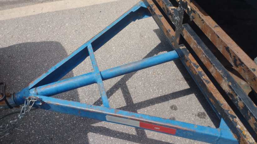 Detalhe da estrutura de um reboque com suporte azul e cabo de segurança, estacionado em uma rua de asfalto.
