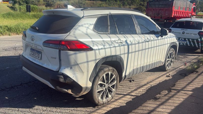 Vista lateral de um SUV branco estacionado em uma estrada, com sujeira visível na lataria, refletores de luz e sombras projetadas sobre ele.
