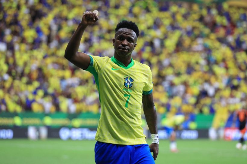 A football player wearing a yellow Brazil national team jersey with the number 7 raises his fist in celebration, surrounded by a crowd displaying yellow team colors.
