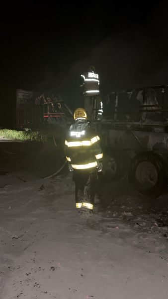 Bombeiros combatendo um incêndio em um caminhão durante a noite, com fumaça visível no ambiente.