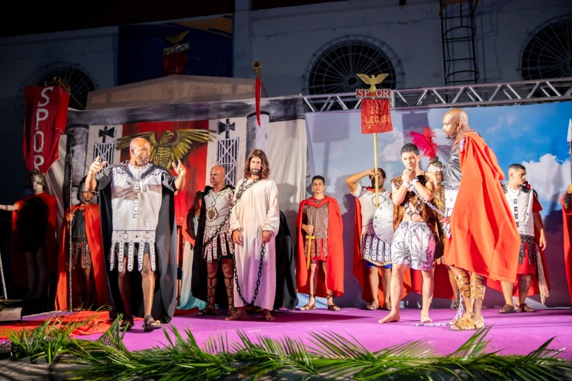 Cenas de uma apresentação teatral com atores vestidos de romanos, incluindo um Jesus e soldados, em um palco decorado com elementos do período.