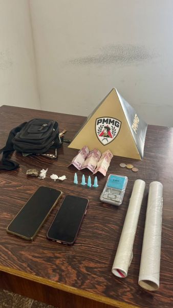 Mesa com objetos diversos incluindo dinheiro, celulares, embalagens e uma placa da PMMG.