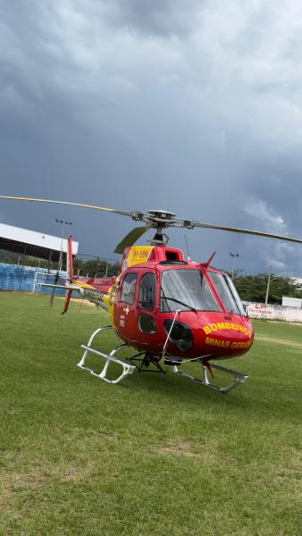 Helicóptero dos Bombeiros de Minas Gerais pousado em um campo, com céu nublado ao fundo.