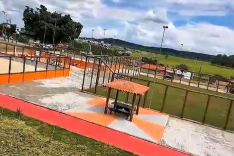 Área de lazer ao ar livre com cercas e pisos coloridos, incluindo uma cabana e vista para um campo verde.