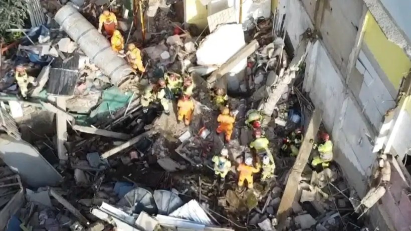 Equipes de resgate trabalhando em meio a destroços de um edifício colapsado, com bombeiros e profissionais de emergência utilizando equipamentos de segurança.