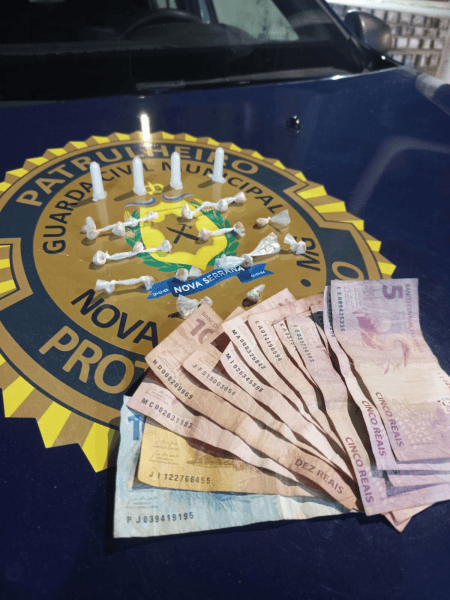 An arrangement of white pills and cash on a police vehicle emblem, featuring Brazilian currency, including five and ten reais notes.