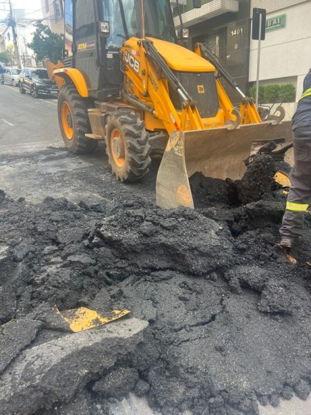 Máquina retroescavadeira JCB trabalhando em a reforma de rua, removendo asfalto em um trecho danificado.