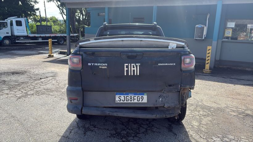 Foto traseira de uma caminhonete Fiat Strada Endurance estacionada em um local com pavimento de asfalto, mostrando detalhes do veículo e placa de identificação.