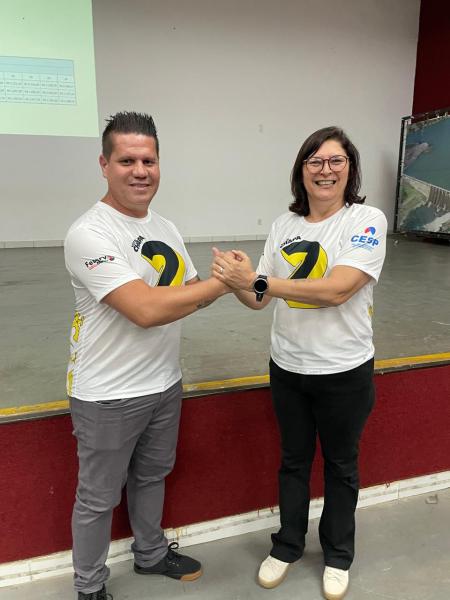 Dois participantes sorrindo e apertando as mãos em um evento, vestindo camisetas brancas com o número 2.