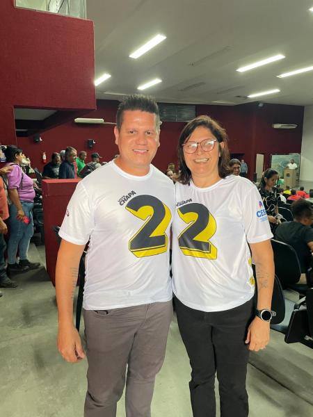 Homem e mulher sorrindo em um ambiente interno, ambos vestindo camisetas brancas com o número 22 estampado em destaque.