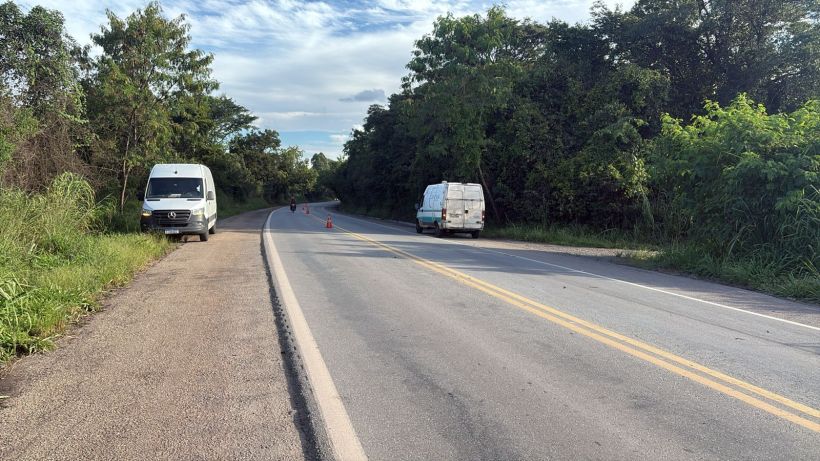 Um trecho de estrada com vans estacionadas, rodeada por vegetação e sinalização de cones.