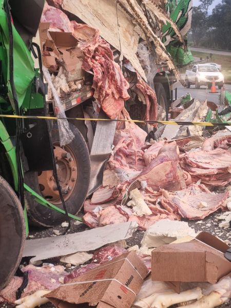 Acidente envolvendo caminhão com carga de carne espalhada na estrada, com caixas vazias e partes do caminhão danificadas.