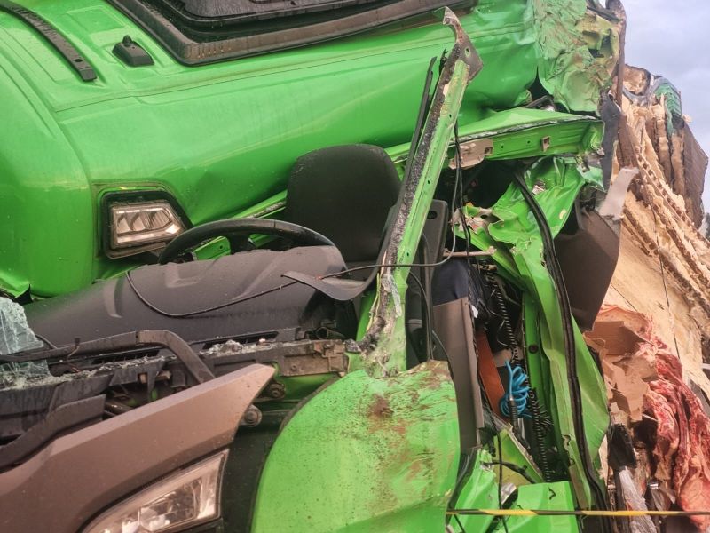 Caminhão verde com danos significativos após um acidente, mostrando a cabine e os componentes internos danificados.