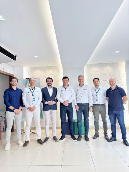 Grupo de seis homens em um ambiente moderno, todos vestidos de maneira profissional, sorrindo para a câmera.