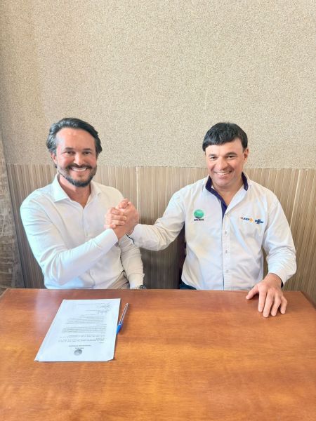 Dois homens sorrindo e apertando as mãos em um ambiente de escritório, com documentos sobre a mesa.