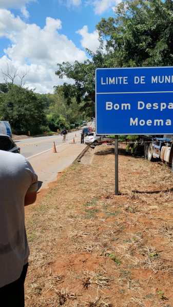 Placa indicando o limite de município entre Bom Despacho e Moema em uma estrada com vegetação ao fundo.