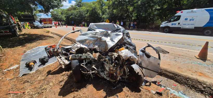 Veículo acidentado em estrada, com a frente gravemente danificada e equipe de emergência ao fundo.