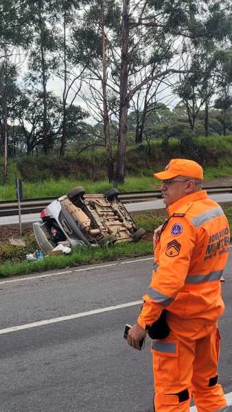Um veículo capotado na beira da estrada com um agente de resgate em traje laranja observando a cena.