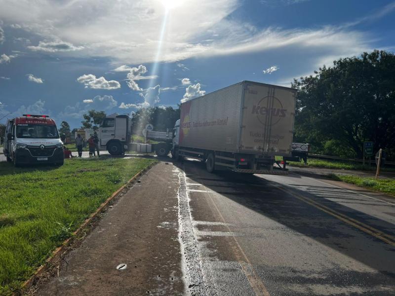 Caminhão parado em uma estrada, com veículos de emergência e pessoas ao redor, sob um céu azul com nuvens.