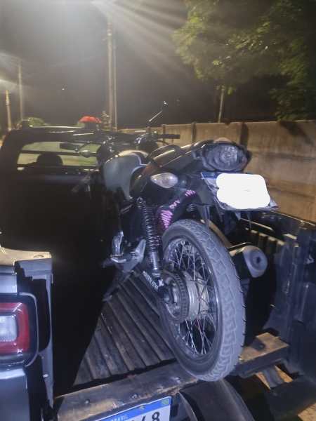 Uma motocicleta preta com detalhes vermelhos sendo transportada na parte traseira de uma caminhonete à noite.