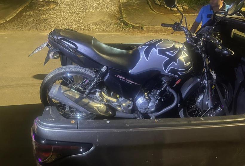 Uma motocicleta preta com detalhes em prata está estacionada na traseira de um carro.
