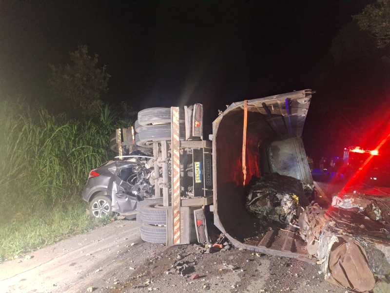 Acidente de trânsito à noite envolvendo um caminhão tombado e um carro danificado na estrada.