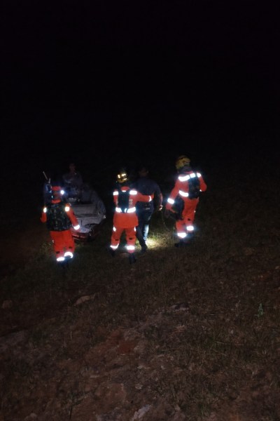 Equipes de resgate vistindo uniformes refletivos, auxiliando em uma operação noturna em área rural.