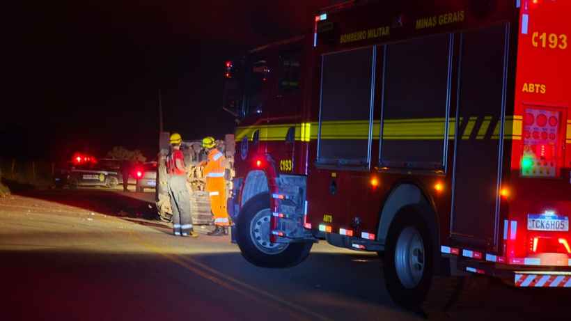 Veículo de bombeiros estacionado em uma estrada à noite, com equipes de resgate em atividade.