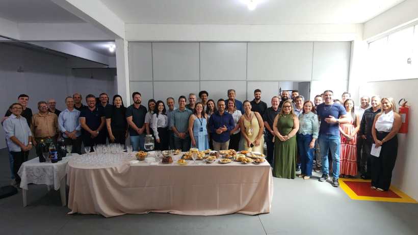 Grupo de pessoas posando para uma foto, com uma mesa de alimentos e bebidas ao fundo, em um ambiente iluminado.