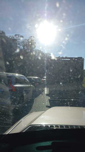 Imagem de um trânsito lento em uma estrada, com veículos acumulados e sol forte ao fundo.