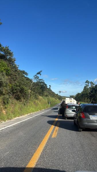 Trânsito lento em uma estrada cercada por vegetação, com carros parados à frente.