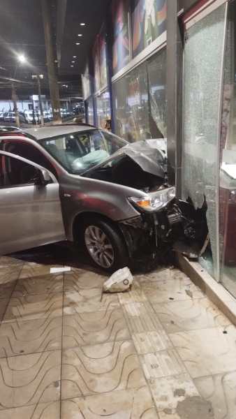 Um carro prata colidiu com a vitrine de um estabelecimento, com o capô danificado e o vidro quebrado.