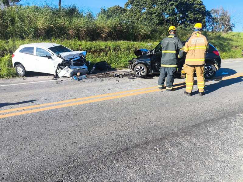 Acidente automobilístico com dois carros envolvidos, um deles bastante danificado, e bombeiros prestando assistência na estrada.