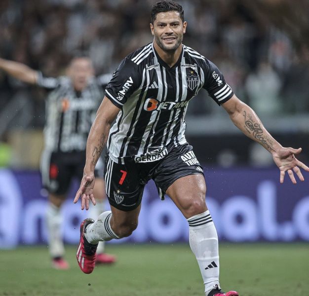 A soccer player celebrating a goal on the field, wearing a black and white striped jersey with the number 7.